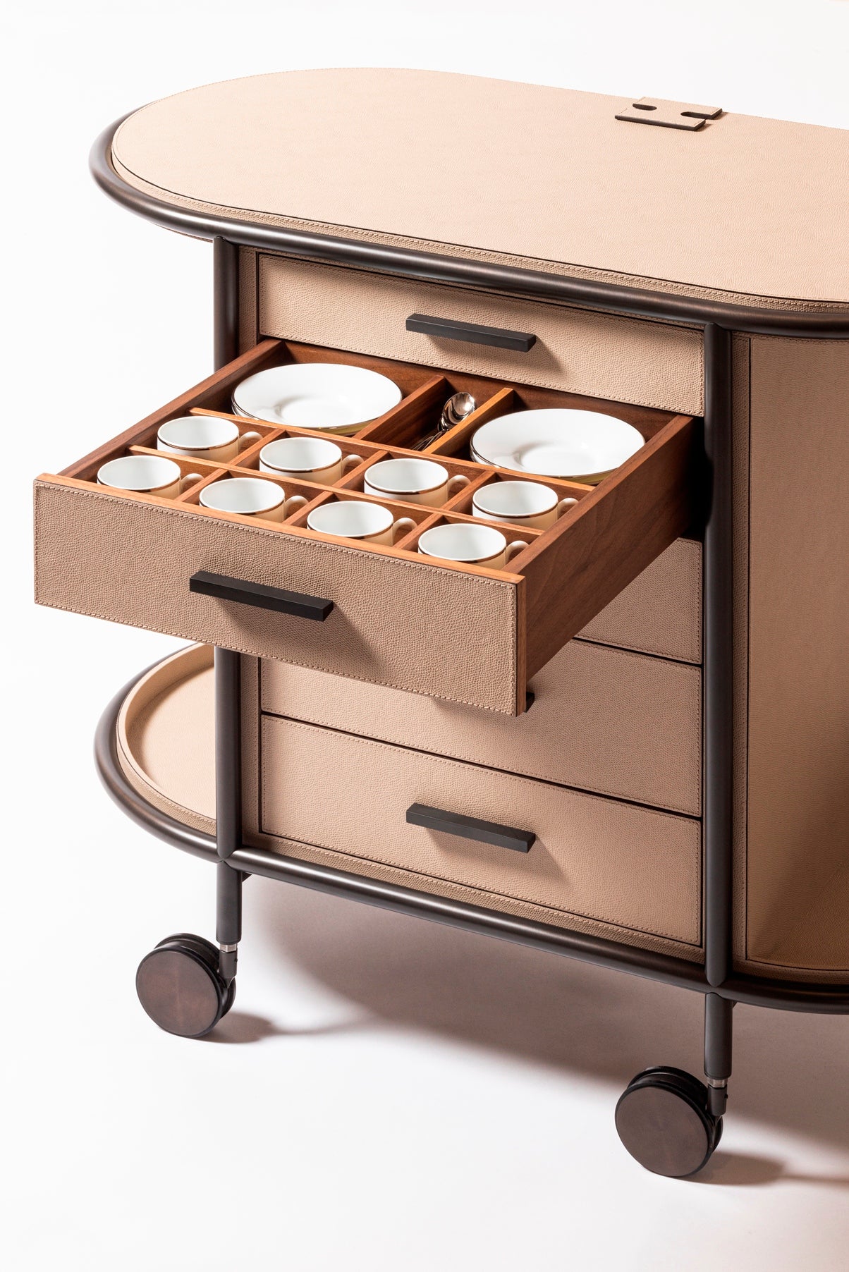 Giobagnara Arcade Coffee and Tea Cart Oval | Leather-covered four-wheel wooden structure with a metal frame and wheels available in three finishes | Features five drawers with sleek metal handles for organized storage of coffee capsules and tea bags | Includes a luxurious set of porcelain coffee and tea cups with matching plates, leather service trays, and coasters | Designed for mobility, combining functionality and sophistication | Furniture and Serveware | 2Jour Concierge, your luxury lifestyle shop