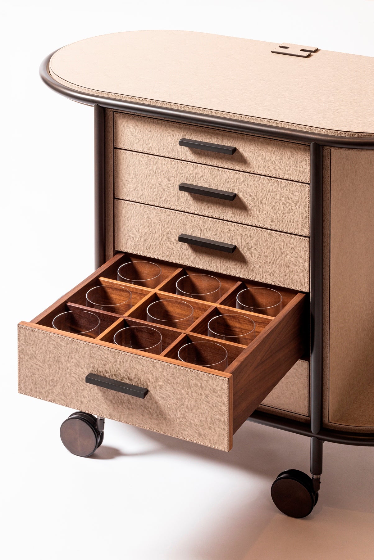 Giobagnara Arcade Coffee and Tea Cart Oval | Leather-covered four-wheel wooden structure with a metal frame and wheels available in three finishes | Features five drawers with sleek metal handles for organized storage of coffee capsules and tea bags | Includes a luxurious set of porcelain coffee and tea cups with matching plates, leather service trays, and coasters | Designed for mobility, combining functionality and sophistication | Furniture and Serveware | 2Jour Concierge, your luxury lifestyle shop