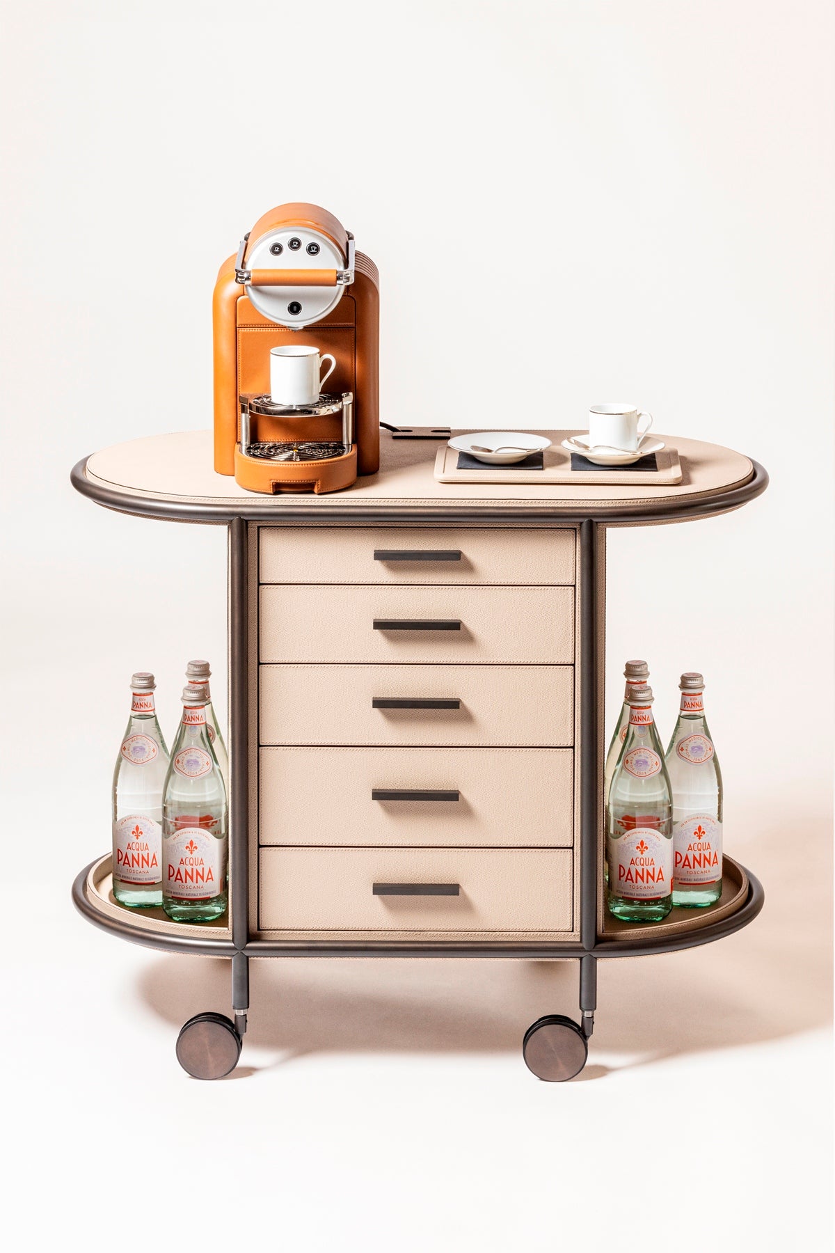 Giobagnara Arcade Coffee and Tea Cart Oval | Leather-covered four-wheel wooden structure with a metal frame and wheels available in three finishes | Features five drawers with sleek metal handles for organized storage of coffee capsules and tea bags | Includes a luxurious set of porcelain coffee and tea cups with matching plates, leather service trays, and coasters | Designed for mobility, combining functionality and sophistication | Furniture and Serveware | 2Jour Concierge, your luxury lifestyle shop