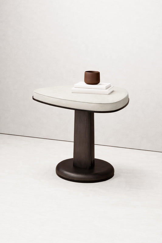 Features: Side table with soft triangular top; leather-wrapped surface; central wooden pedestal base; metal edge outlining the top; compact proportions; suitable for residential and hospitality use