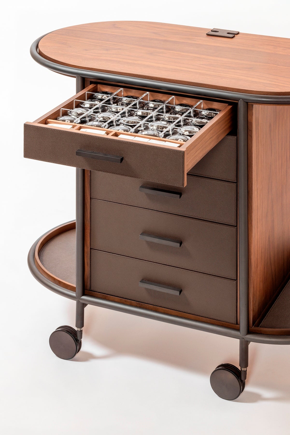 Giobagnara Arcade wood coffee and tea cart oval | Refined coffee and tea cart with a four-wheel structure in natural, walnut, or wenge wood | Metal frame and wheels available in chrome, bronze, or brass finishes | Features five organized drawers with sleek metal handles for storing coffee capsules, tea bags, and accessories | Includes porcelain coffee and tea cups with matching plates and silver graphic trim, plus wood trays and coasters | Designed for easy mobility and sophisticated presentation | Perfect 