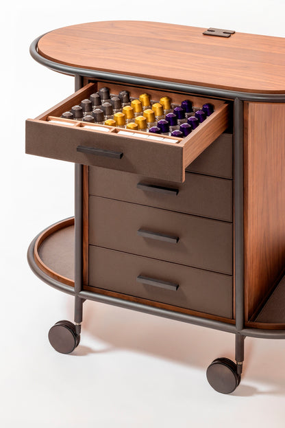 Giobagnara Arcade wood coffee and tea cart oval | Refined coffee and tea cart with a four-wheel structure in natural, walnut, or wenge wood | Metal frame and wheels available in chrome, bronze, or brass finishes | Features five organized drawers with sleek metal handles for storing coffee capsules, tea bags, and accessories | Includes porcelain coffee and tea cups with matching plates and silver graphic trim, plus wood trays and coasters | Designed for easy mobility and sophisticated presentation | Perfect 