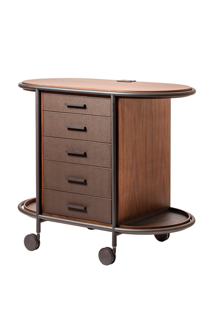 Giobagnara Arcade wood coffee and tea cart oval | Refined coffee and tea cart with a four-wheel structure in natural, walnut, or wenge wood | Metal frame and wheels available in chrome, bronze, or brass finishes | Features five organized drawers with sleek metal handles for storing coffee capsules, tea bags, and accessories | Includes porcelain coffee and tea cups with matching plates and silver graphic trim, plus wood trays and coasters | Designed for easy mobility and sophisticated presentation | Perfect 